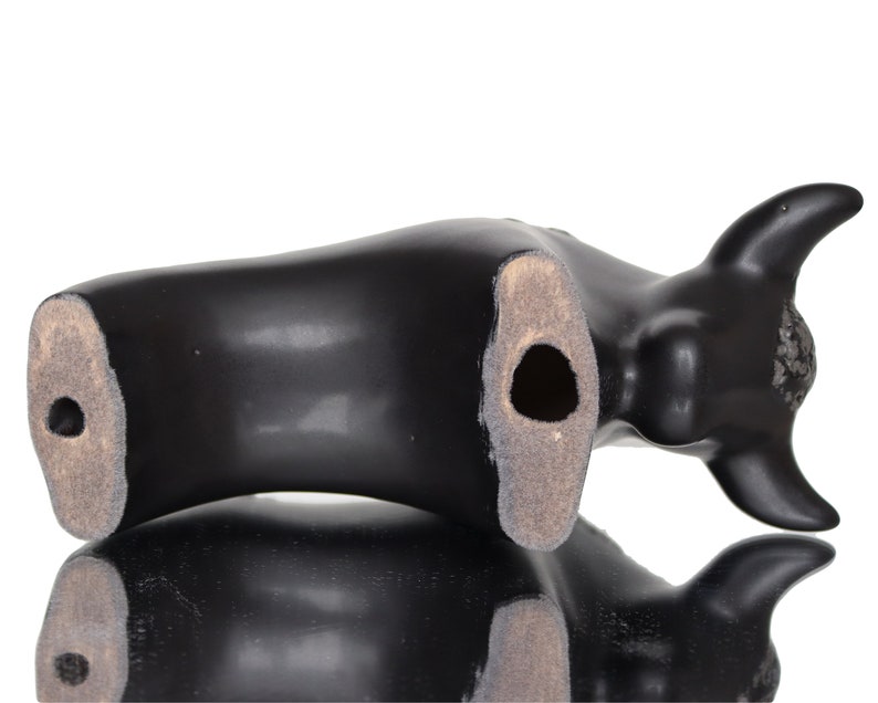 May include: Black ceramic bull figurine with a hole in the bottom. The figurine is lying on its side.