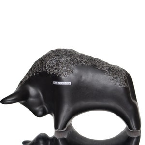 May include: Black ceramic bull sculpture with a textured surface. The sculpture has a label that reads "D.T.O. Keramik".
