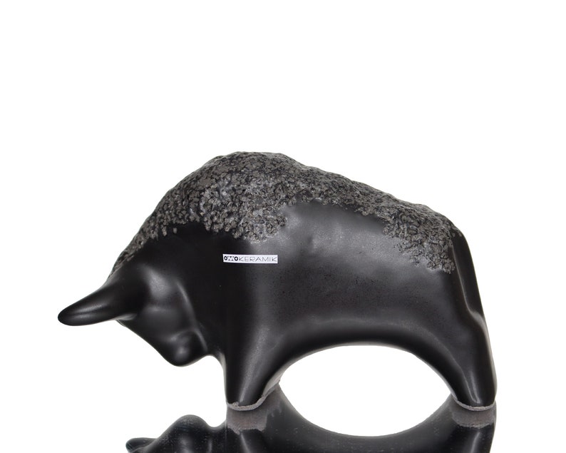 May include: Black ceramic bull sculpture with a textured surface. The sculpture has a label that reads "D.T.O. Keramik".