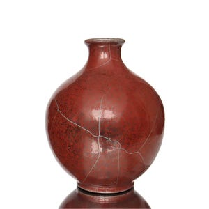 Può includere: Un vaso in ceramica rotondo e bulboso con una finitura smaltata rosso scuro lucido. La superficie presenta una rete distinta di sottili crepe bianche che si estendono sul corpo del recipiente, dotato di un collo stretto e una piccola apertura.
