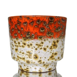 May include: A ceramic planter with a vibrant orange top and a speckled white base. The planter has a unique, textured glaze and a pedestal base. This decorative piece is suitable for indoor or outdoor use.