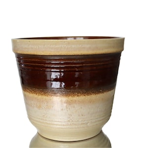 Peut inclure: Un pot en céramique émaillée brun et crème avec un bord large et une base arrondie.