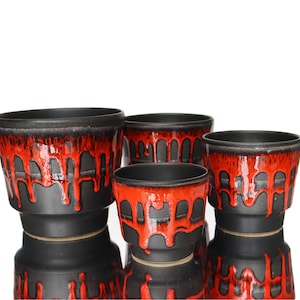 May include: A collection of four ceramic plant pots in different sizes. The pots are black with a striking red, dripped glaze pattern. These pots have a mid-century modern style, suitable for indoor or outdoor use.