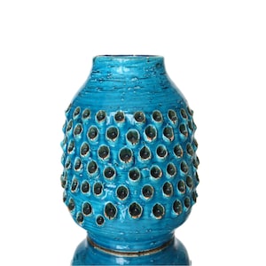 May include: A turquoise ceramic vase with a textured surface and a pattern of raised, rounded bumps. The vase has a wide base and a narrower neck, with dark recesses within the bumps. The design is reminiscent of a sea urchin.