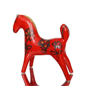 Può includere: Una statuetta di cavallo in ceramica rossa lucida caratterizzata da un motivo floreale nero dipinto a mano sul corpo. Il cavallo presenta una superficie liscia e riflettente, un collo curvo e una coda corta e dritta, poggiante su quattro zampe.
