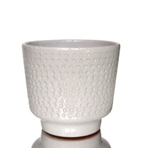 Peut inclure: Un cache-pot en céramique blanche avec une finition brillante et un motif en losanges gaufrés répété sur l'extérieur. Le récipient présente une large ouverture supérieure qui se rétrécit vers une base circulaire plus étroite et étagée.