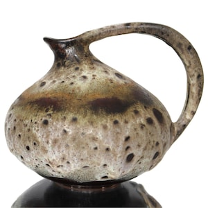 May include: A brown and white ceramic pitcher with a speckled glaze and a wide, rounded body. The pitcher has a brown handle and a dark brown base.