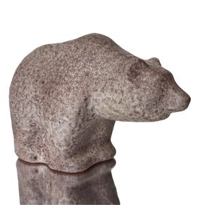 May include: A ceramic bear sculpture with a speckled brown and white glaze. The bear is standing on all fours with its head tilted down.