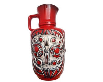 Puede incluir: Jarrón de cerámica rojo con un diseño floral blanco y negro. El jarrón tiene una boca ancha y un asa.