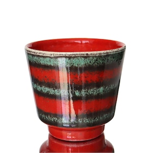 Peut inclure: Pot de fleurs en céramique à rayures rouges et noires, avec une base en piédestal. Le pot a une finition brillante et un intérieur rouge. Les rayures sont horizontales, avec des bandes alternées de rouge, de noir et de vert.