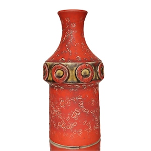 Pode incluir: Um vaso de cerâmica alto e cilíndrico com um acabamento vermelho mate vibrante e uma superfície texturizada e manchada. A secção superior apresenta uma faixa horizontal decorada com uma série de motivos circulares em relevo em tons de dourado e vermelho.