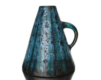 May include: A teal and dark blue ceramic vase with a handle. The vase has a unique shape, wider at the base and tapering upwards. The glaze has a textured, speckled appearance with dark streaks.