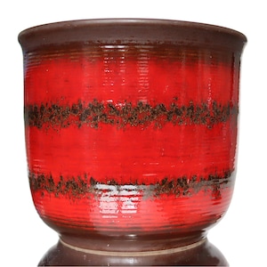 Op de afbeelding: Een rode en bruine keramische plantenpot met een geometrisch patroon. De pot heeft een brede basis en een smalle bovenkant.