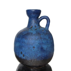 May include: A blue ceramic vase with a rounded body, a small handle, and a narrow neck. The vase has a dark blue base that fades into a lighter blue with a textured appearance. The vase is likely for decorative purposes.