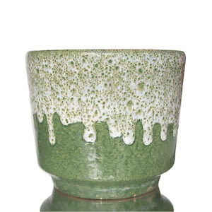 Può includere: Un vaso di ceramica verde con una glassa bianca che cola sui lati. Il vaso ha una superficie testurizzata e una base larga.