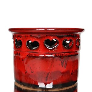 Peut inclure: Pot en céramique rouge avec un motif de découpe en forme de cœur autour du bord supérieur. Le pot a une finition brillante et une surface texturée.