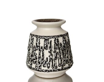 Può includere: Un vaso in ceramica color crema con un motivo nero strutturato. Il vaso ha un corpo arrotondato e un collo stretto. Il bordo e l'interno sono marrone scuro. Il design è un motivo verticale ripetuto di punti e linee nere.