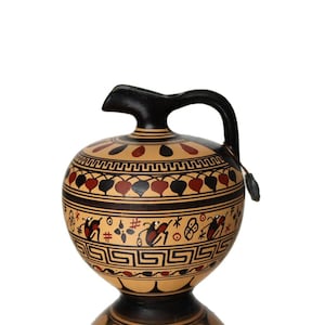 May include: A black-handled, round ceramic jug with a spout. The jug features a beige base with black and red painted designs, including leaf and geometric patterns. The top and handle are black.