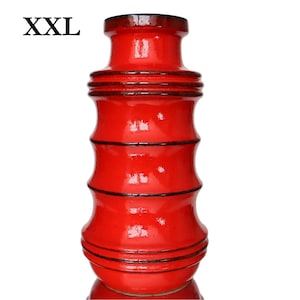 May include: A vibrant red ceramic vase with a distinctive cylindrical form, featuring dark brown accents and horizontal bands. The text "XXL" is visible. This decorative vase, suitable for home decor, is approximately 30 cm tall.
