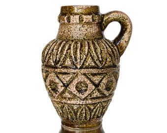 May include: A textured, brown and gold ceramic pitcher with a handle. The pitcher has a detailed, embossed pattern of geometric shapes and lines. The overall design is vintage and decorative.
