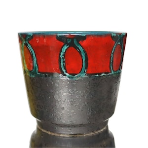 Peut inclure: Un cache-pot en céramique présentant une bande supérieure rouge vif ornée d'un motif ovale bleu sarcelle répétitif. La partie inférieure du récipient est finie avec un vernis gris anthracite texturé, créant un contraste marqué entre les deux.