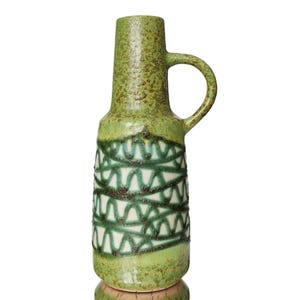 May include: A green ceramic vase with a white and green geometric pattern. The vase has a handle and a textured surface.
