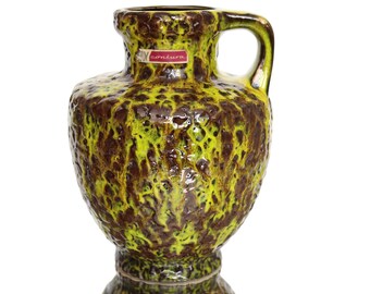 May include: A green and brown ceramic vase with a textured surface and a handle. The vase has a label that says "conturA".