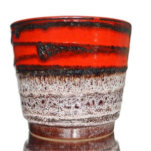 May include: A cylindrical ceramic planter featuring a vibrant orange upper section with horizontal black drip glaze accents, transitioning into a textured white and brown speckled base with a glossy finish and a wide, open top rim.