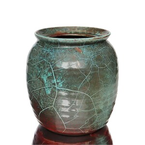 Peut inclure: Un vase en céramique arrondi présentant un vernis bleu sarcelle foncé et brun avec un motif craquelé prononcé sur la surface. Le récipient possède une large ouverture avec un bord légèrement évasé et une finition lisse et brillante.