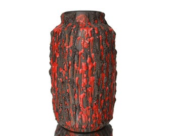 May include: A tall, cylindrical ceramic vase with a textured, lava-like surface. The vase features a dark brown base color with vibrant red accents that drip down the sides. The top rim is a solid dark brown.