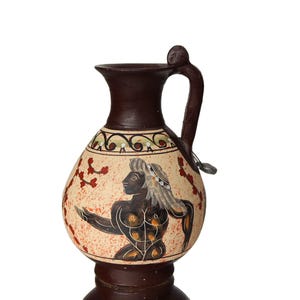 May include: A brown ceramic vase with a handle and a painted design of a person with a crown. The vase has a cream background with red and green accents.
