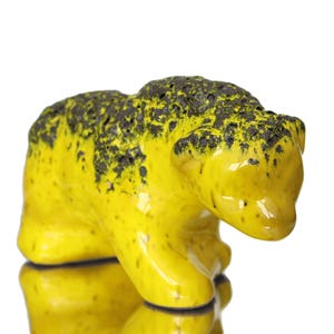 Könnte beinhalten: Keramik-Bärenfigur mit leuchtend gelber Glasur und dunklen, gesprenkelten Akzenten. Der Bär ist in einer geduckten Position dargestellt, mit glänzendem Finish. Die Figur ist ein dekorativer Artikel.