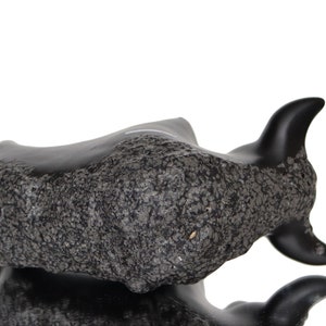 May include: Black ceramic bull sculpture with a rough, textured surface. The bull is lying down with its head turned to the side.