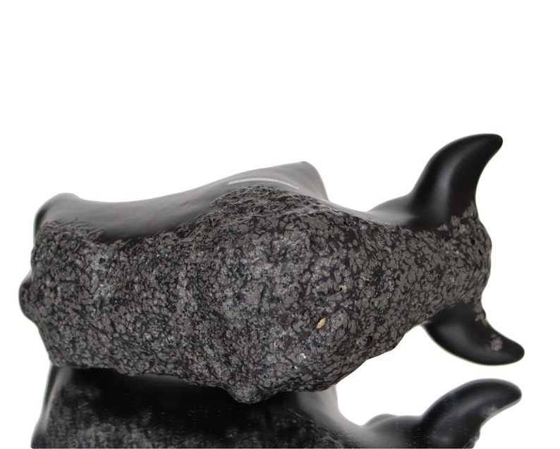 May include: Black ceramic bull sculpture with a rough, textured surface. The bull is lying down with its head turned to the side.
