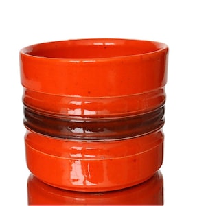 Könnte beinhalten: Ein zylindrischer Keramikbehälter mit glänzender orangefarbener Glasur. Das Design weist horizontale Rillen und ein dunkelbraunes Band auf. Der Behälter spiegelt sich in der darunter liegenden Oberfläche.