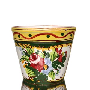 Op de afbeelding: Handbeschilderde keramische bloempot met een witte basis. De pot heeft een gele rand met rode en groene accenten, een groene band en een bloemenontwerp met rode, groene en blauwe bloemen. Geschikt voor binnen of buiten.