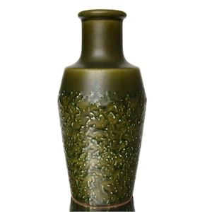 May include: A tall, olive green ceramic vase with a textured, organic pattern on the lower portion. The vase has a smooth, cylindrical neck and a slightly flared base. The overall design is simple and elegant.