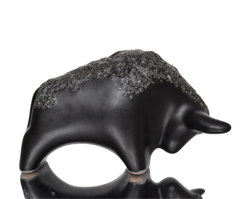 May include: Black ceramic bull figurine with a textured surface. The bull is standing on its four legs with its head turned to the side.