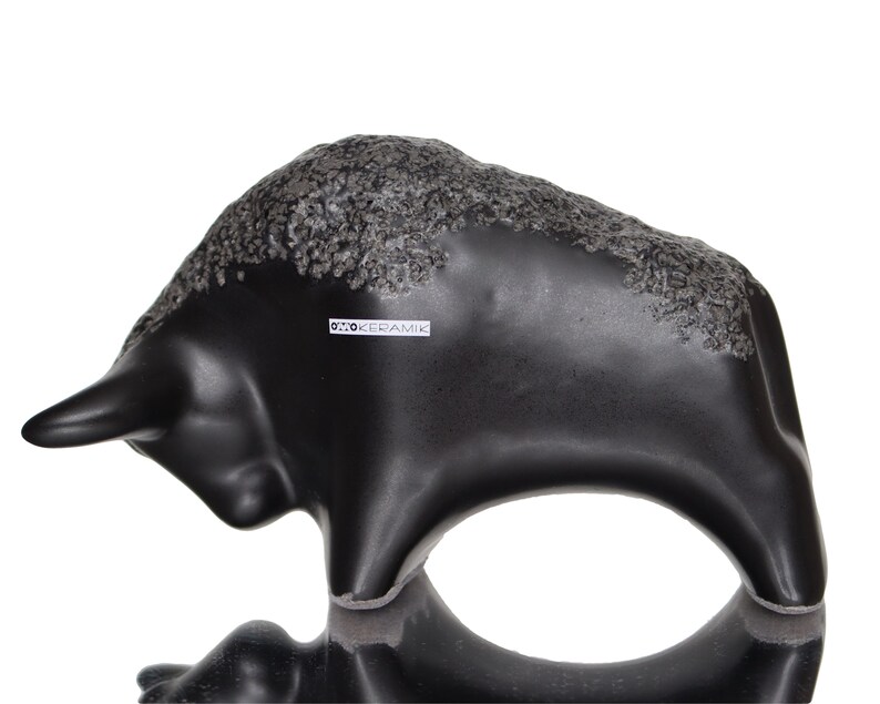 May include: Black ceramic bull sculpture with a textured surface. The sculpture is signed "Otto Keramik" on the side.