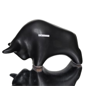 May include: A black bull sculpture with a smooth, glossy finish. The bull is depicted in a charging pose. The sculpture is likely made of a solid material and has a reflective surface. The sculpture is a decorative item.