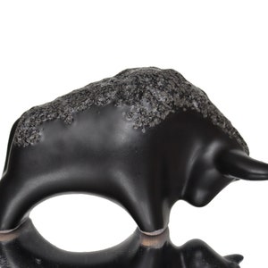 May include: Black ceramic bull figurine with a textured surface. The bull is standing on its four legs with its head turned to the side.
