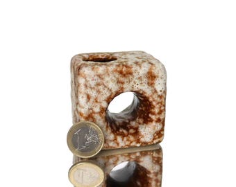 May include: A square, ceramic vase with a hole through the center. The vase has a speckled brown and cream color. A one Euro coin is next to the vase for size comparison.