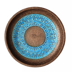 May include: A round, brown ceramic bowl with a turquoise blue, patterned centre. The bowl's interior features a concentric design, with a central circle and a ring of repeating floral-like motifs in the centre. The exterior is a darker brown.