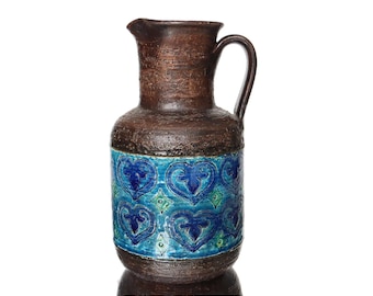 May include: A brown ceramic pitcher with a blue and green geometric pattern. The pitcher has a wide base and a narrow neck with a handle.