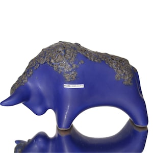 May include: A ceramic sculpture of a bull in a vibrant blue hue, with a textured, dark gray top. The bull's form is stylized, with a smooth, glossy finish. The sculpture has the text "OKOKERAMIK".