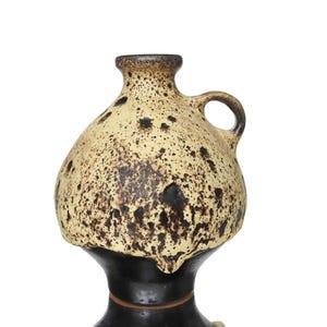 May include: A ceramic jug featuring a bulbous upper section with a cream-colored glaze and dark brown speckled texture. The lower portion is a smooth, solid black base. A small handle is attached to the side of the neck, which has a flared rim.