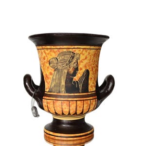 Könnte beinhalten: Eine schwarze und orangefarbene Keramikvase mit einem griechischen Design, das das Profil einer Frau zeigt. Die Vase hat zwei Henkel und einen runden Boden.