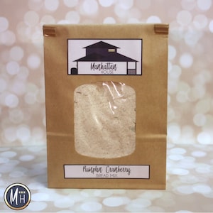 May include: A brown paper bag of Pumpkin Cranberry Bread Mix from Manhattan House. The bag has a clear window showing the mix inside. The Manhattan House logo and product name are printed on the bag.