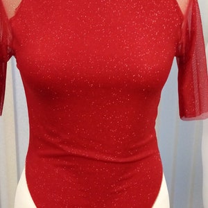 May include: A red sequined top with a mesh overlay on the sleeves. The top has a scoop neckline and a fitted silhouette.