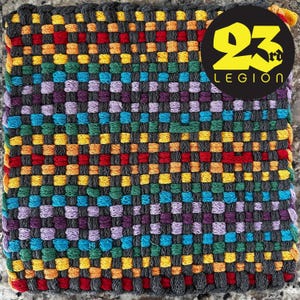 May include: A woven square rug with a colorful checkered pattern in shades of red, yellow, blue, green, and purple. The rug is made with thick yarn and has a textured surface. The rug is surrounded by a black border.
